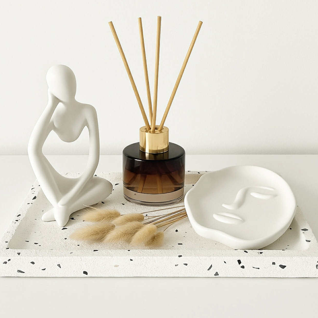 Decorative items including a ceramic figure, diffuser, and face-shaped dish on a white surface.